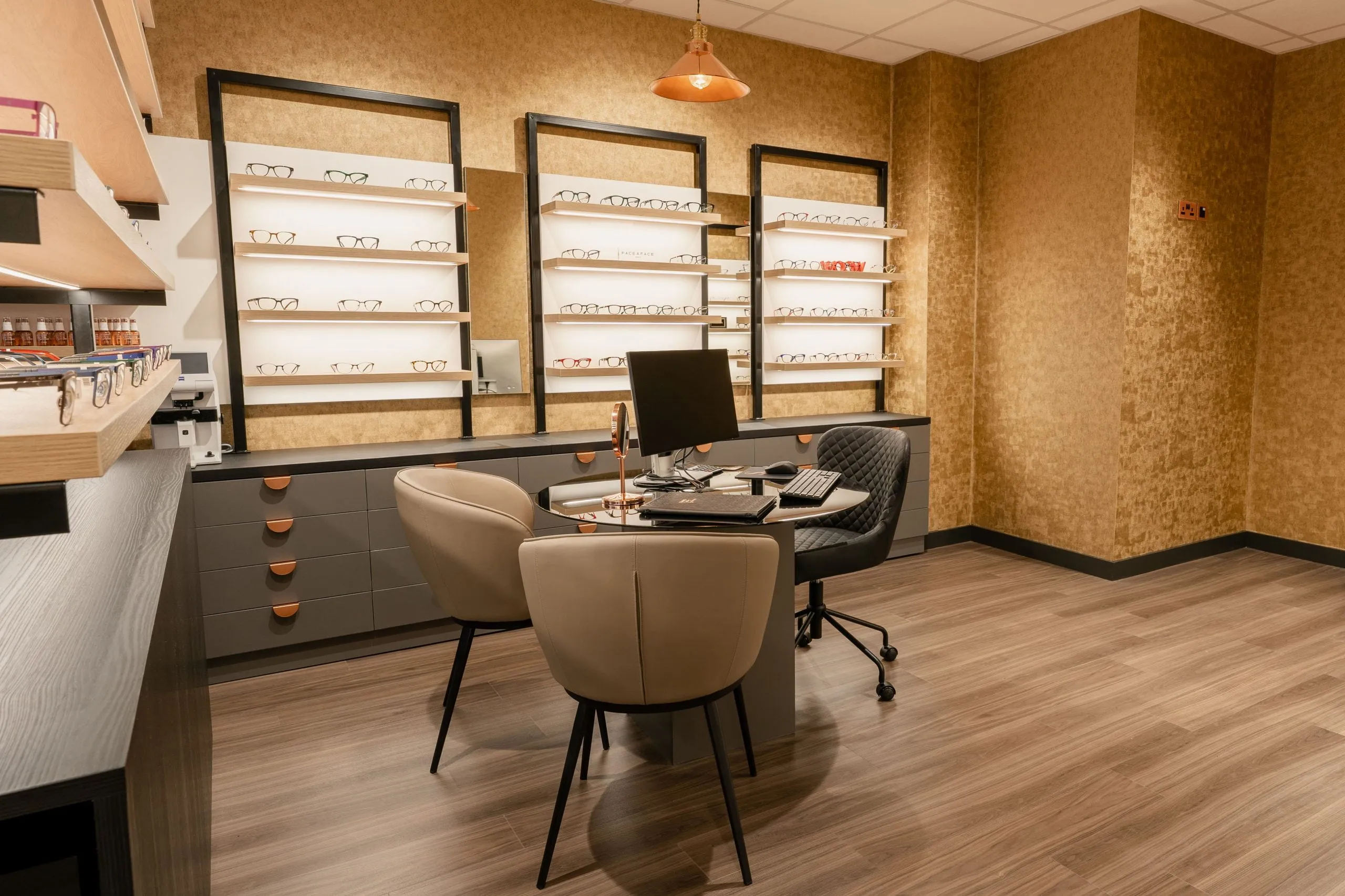 A consulting desk in front of lit frame shelves and gold wallpaper at the practice