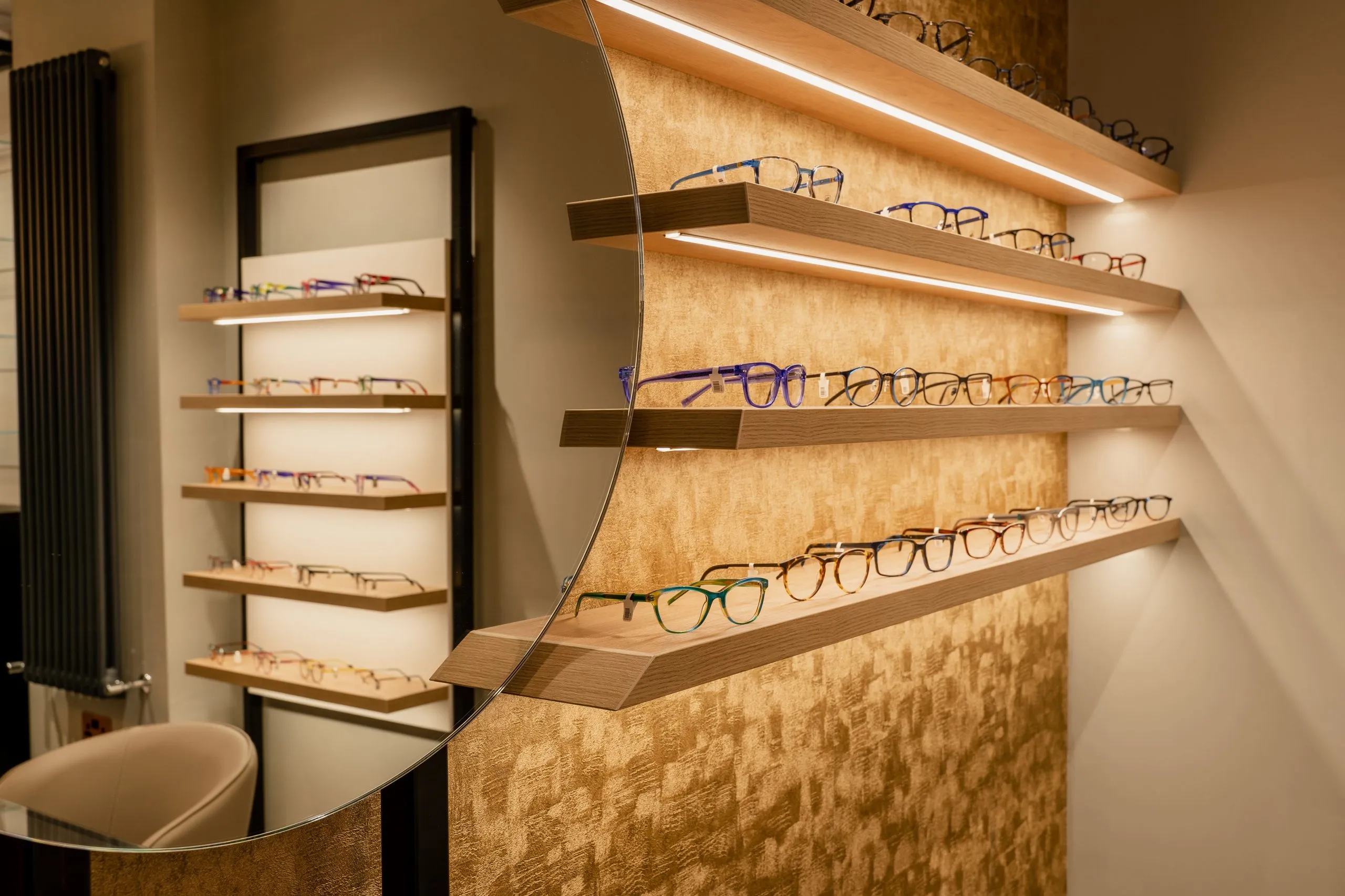 Frames on lit oak shelves beside a round mirror