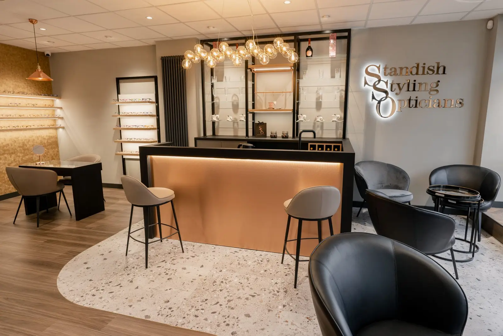 Inside Standish Styling Opticians: the copper-fronted bar, velvet chairs on a terrazzo floor, and the illuminated sign